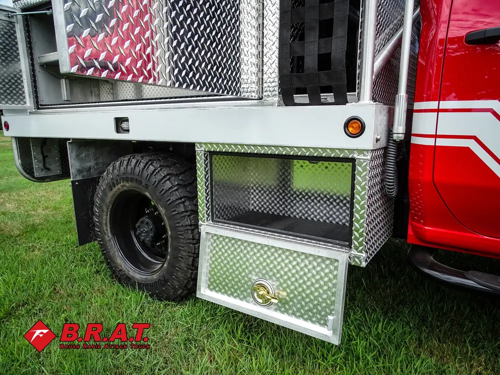 Exterior view of small fire truck showing cab, body compartments, and wheel/tire area.