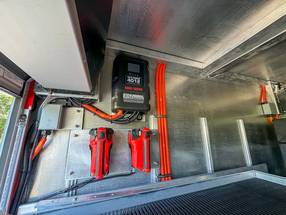 Compartment close-up with mounted charger, extinguisher, and wiring.