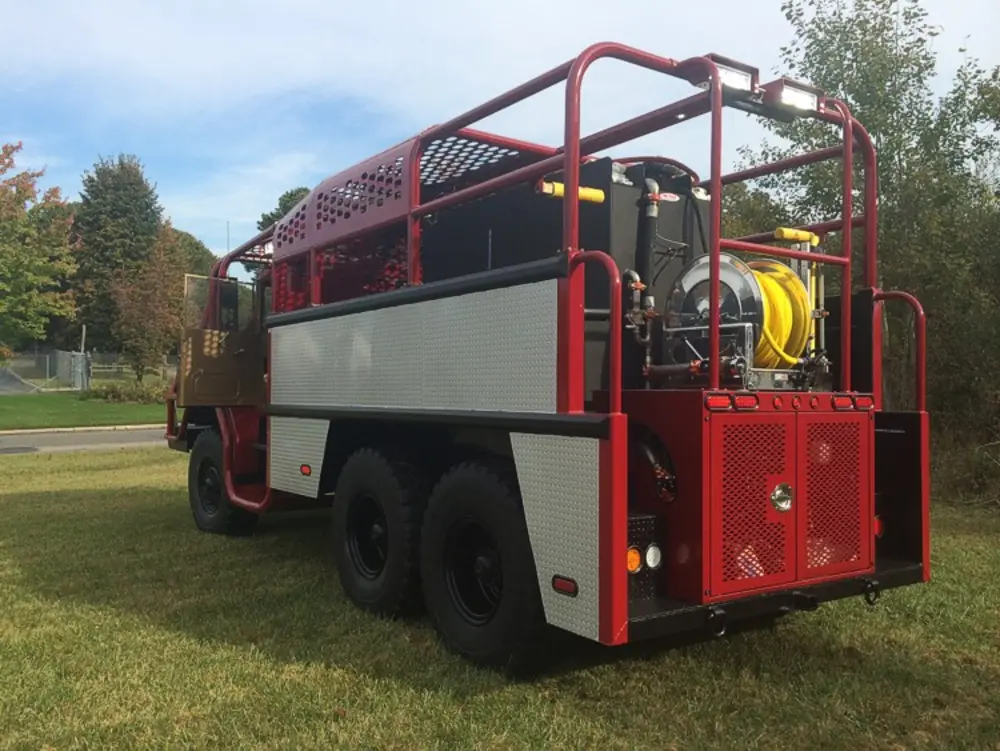Exterior view of small fire truck showing cab, body compartments, and wheel/tire area.