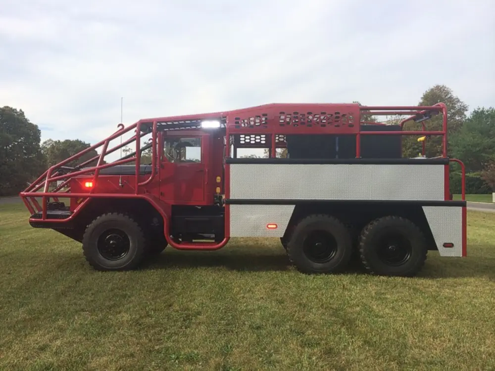 Exterior view of small fire truck showing cab, body compartments, and wheel/tire area.