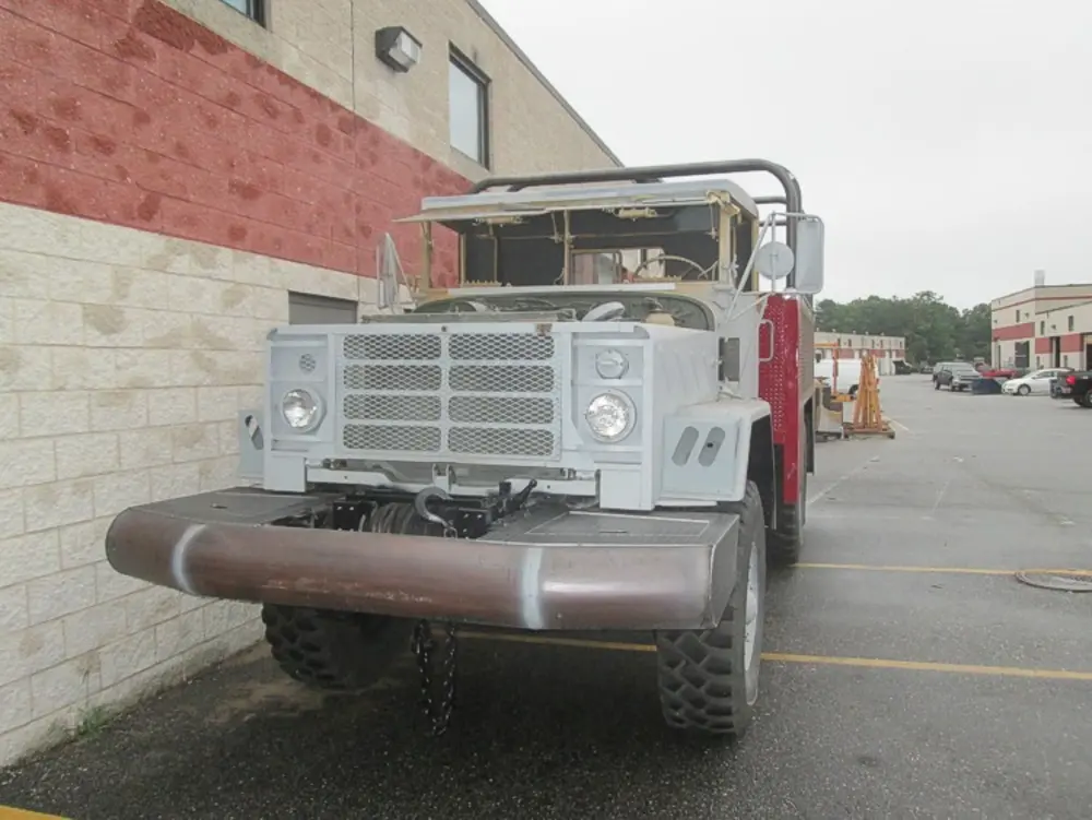 Exterior view of small fire truck showing cab, body compartments, and wheel/tire area.