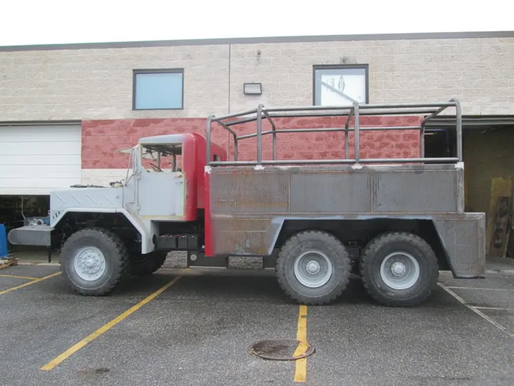 Exterior view of small fire truck showing cab, body compartments, and wheel/tire area.