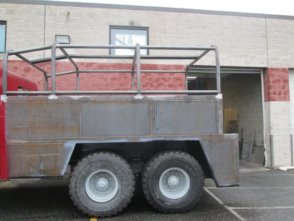 Exterior view of small fire truck showing cab, body compartments, and wheel/tire area.