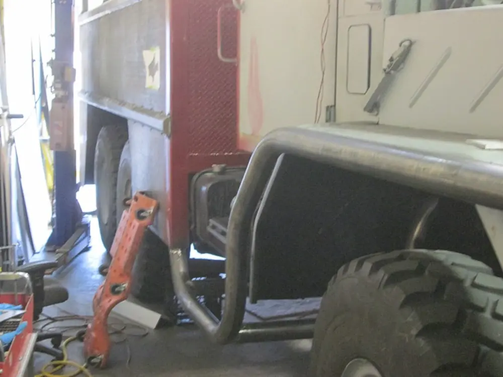 Exterior view of small fire truck showing cab, body compartments, and wheel/tire area.