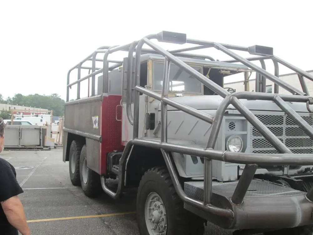 Exterior view of small fire truck showing cab, body compartments, and wheel/tire area.