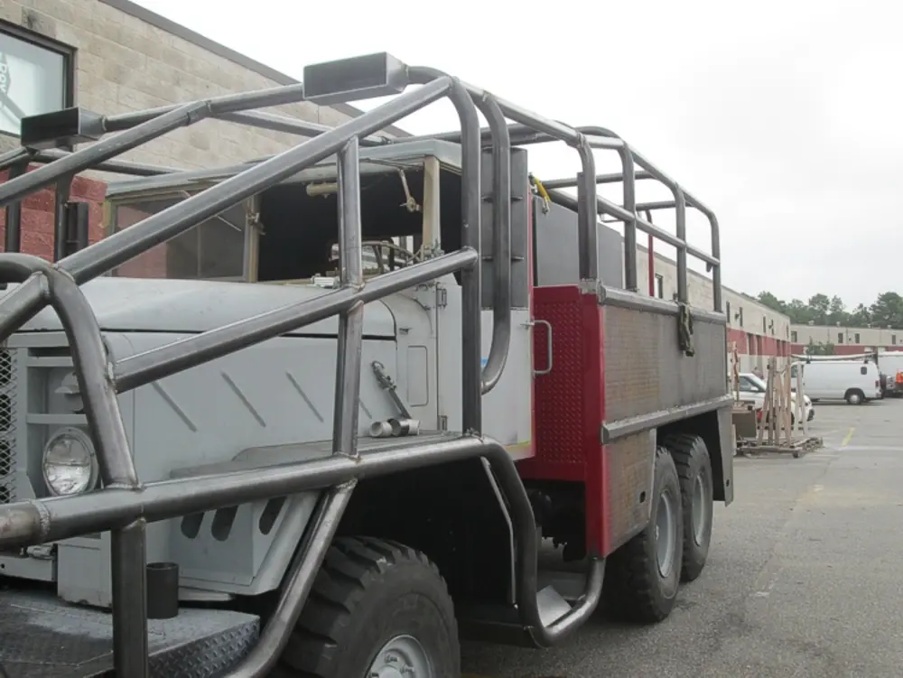Exterior view of small fire truck showing cab, body compartments, and wheel/tire area.
