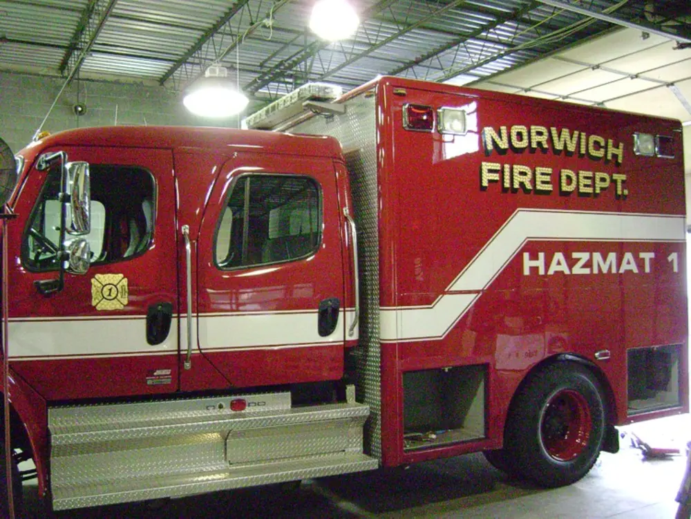 Exterior view of small fire truck showing cab, body compartments, and wheel/tire area.