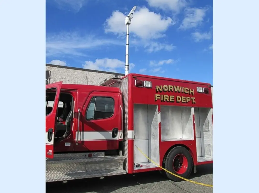 Exterior view of small fire truck showing cab, body compartments, and wheel/tire area.