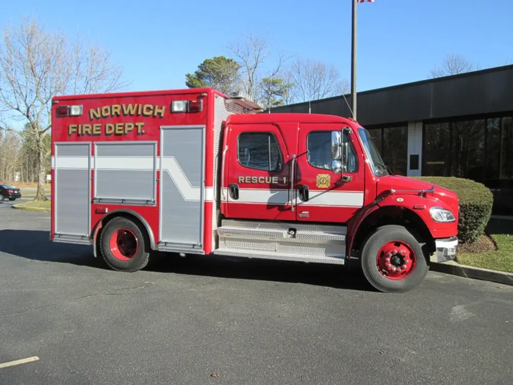 Exterior view of small fire truck showing cab, body compartments, and wheel/tire area.