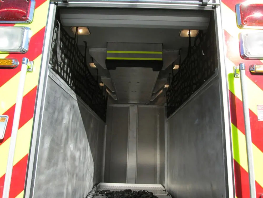 Exterior view of small fire truck showing cab, body compartments, and wheel/tire area.