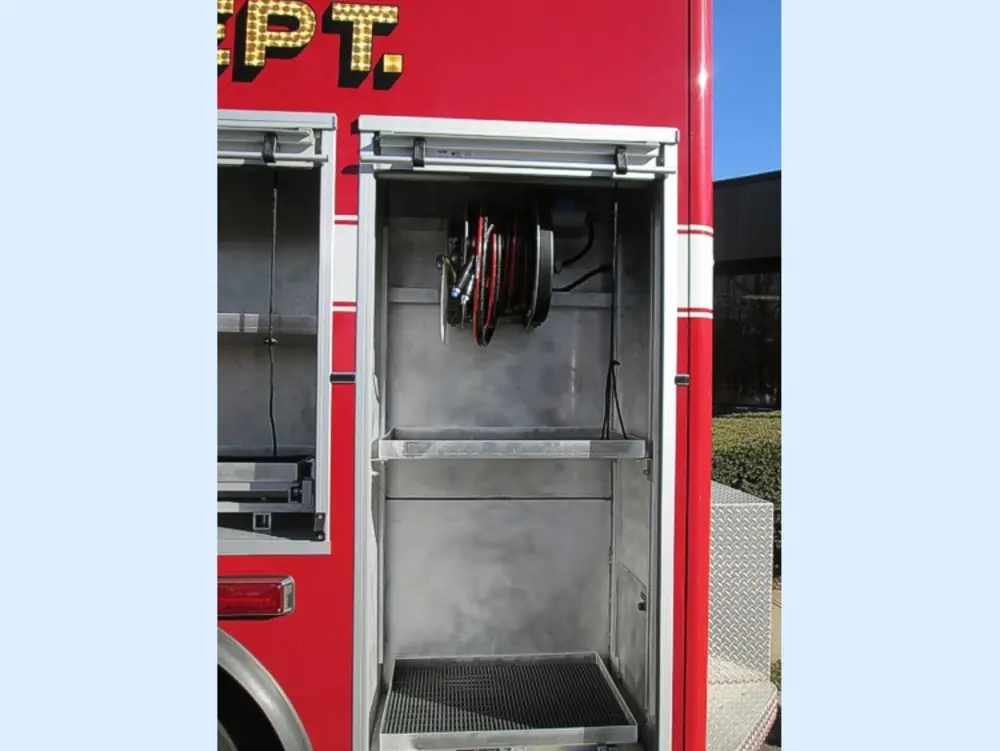 Exterior view of small fire truck showing cab, body compartments, and wheel/tire area.