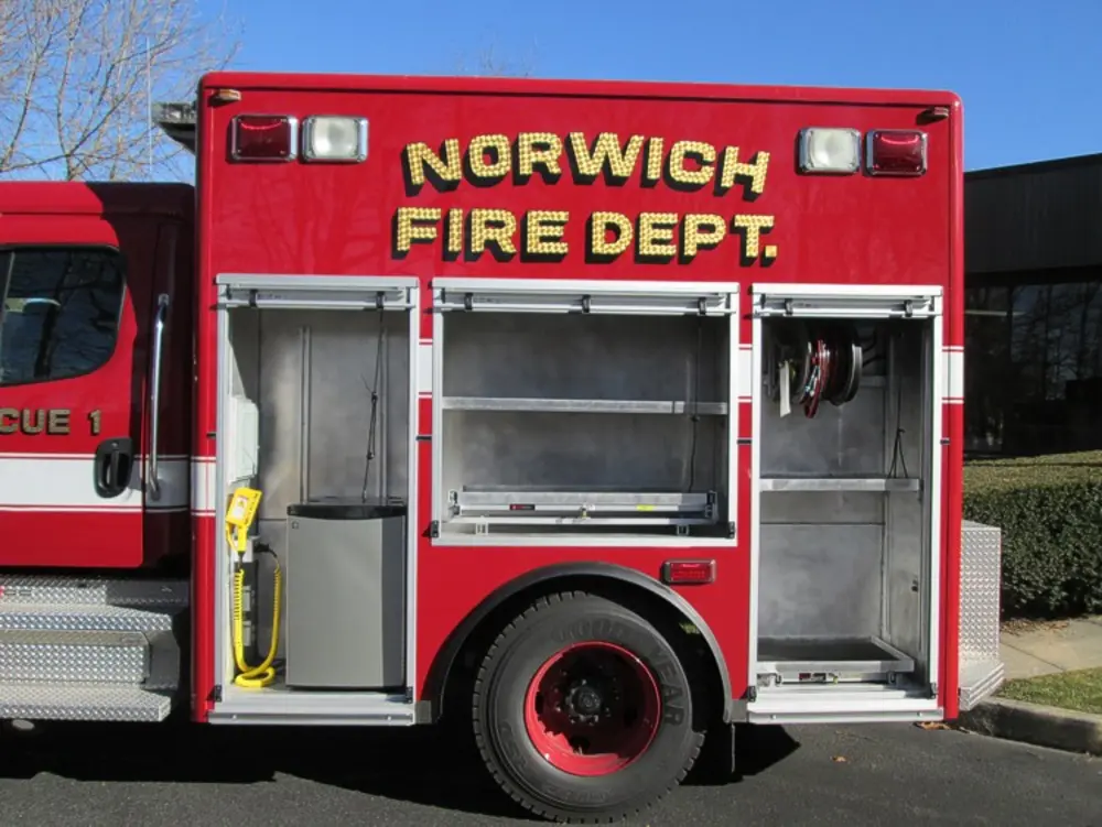 Exterior view of small fire truck showing cab, body compartments, and wheel/tire area.