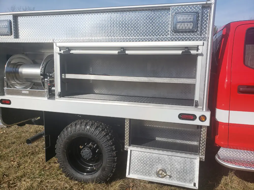 Exterior view of small fire truck showing cab, body compartments, and wheel/tire area.