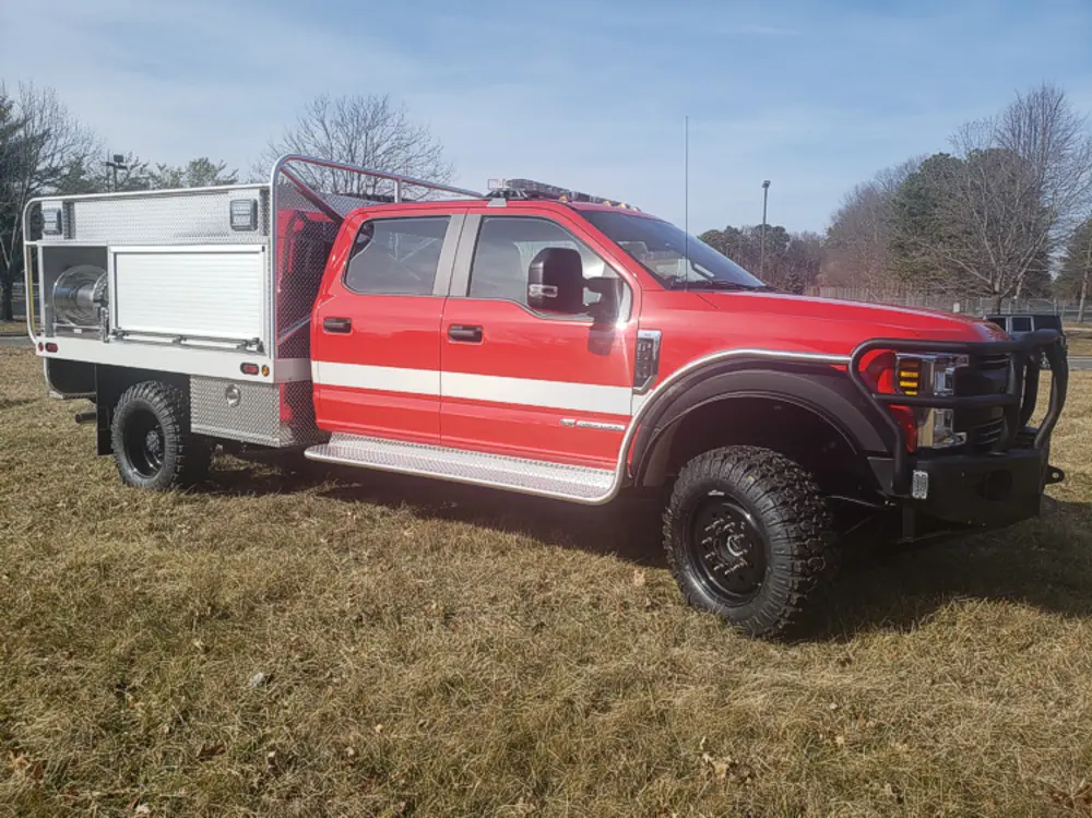 Exterior view of small fire truck showing cab, body compartments, and wheel/tire area.