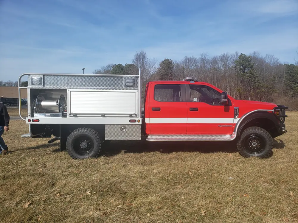 Exterior view of small fire truck showing cab, body compartments, and wheel/tire area.