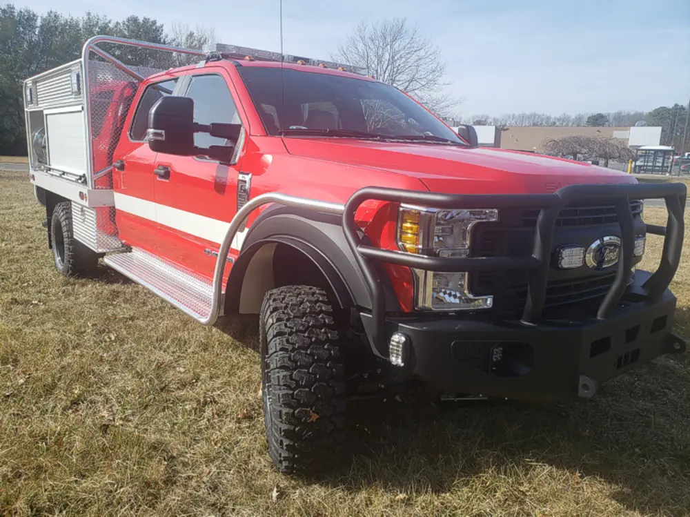 Exterior view of small fire truck showing cab, body compartments, and wheel/tire area.