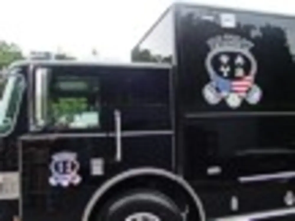 Exterior view of small fire truck showing cab, body compartments, and wheel/tire area.