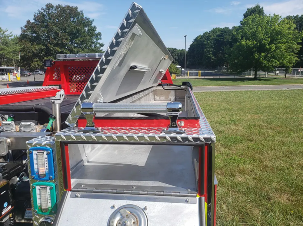 Exterior view of small fire truck showing cab, body compartments, and wheel/tire area.