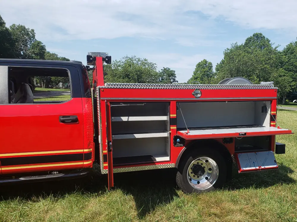 Exterior view of small fire truck showing cab, body compartments, and wheel/tire area.