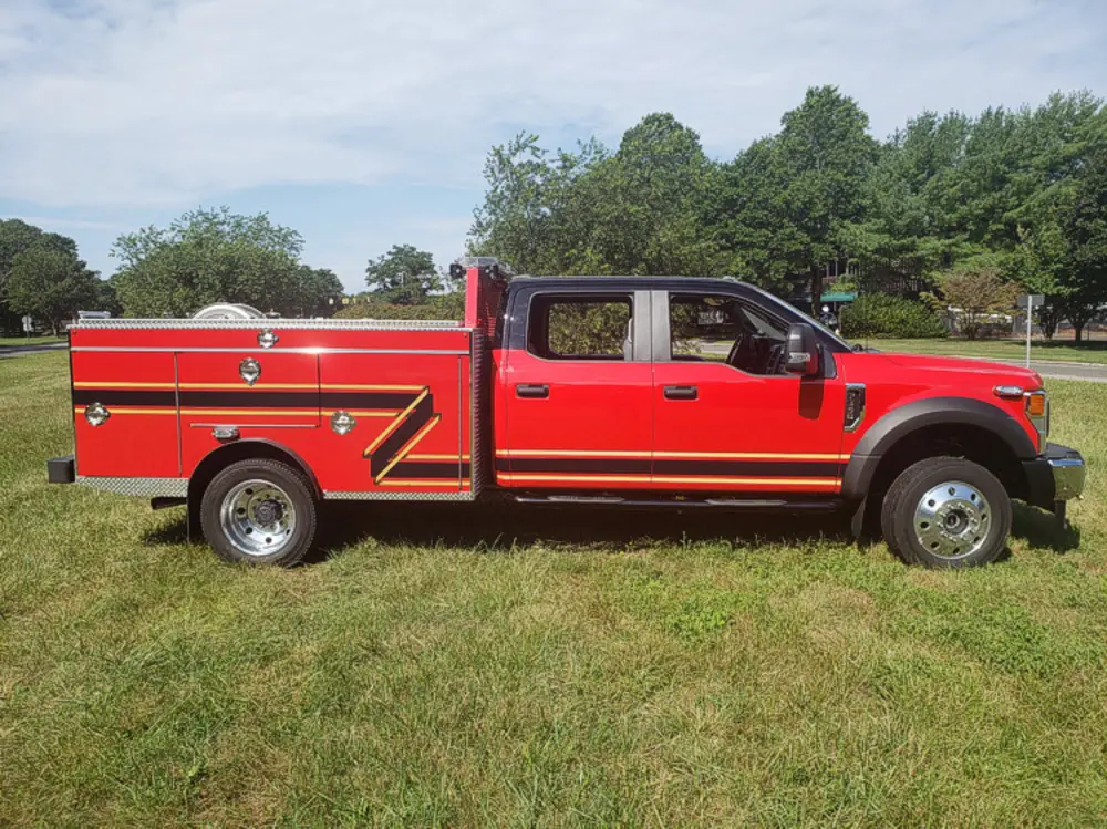 Exterior view of small fire truck showing cab, body compartments, and wheel/tire area.