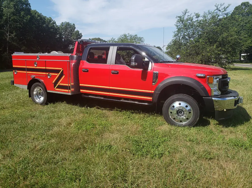 Exterior view of small fire truck showing cab, body compartments, and wheel/tire area.