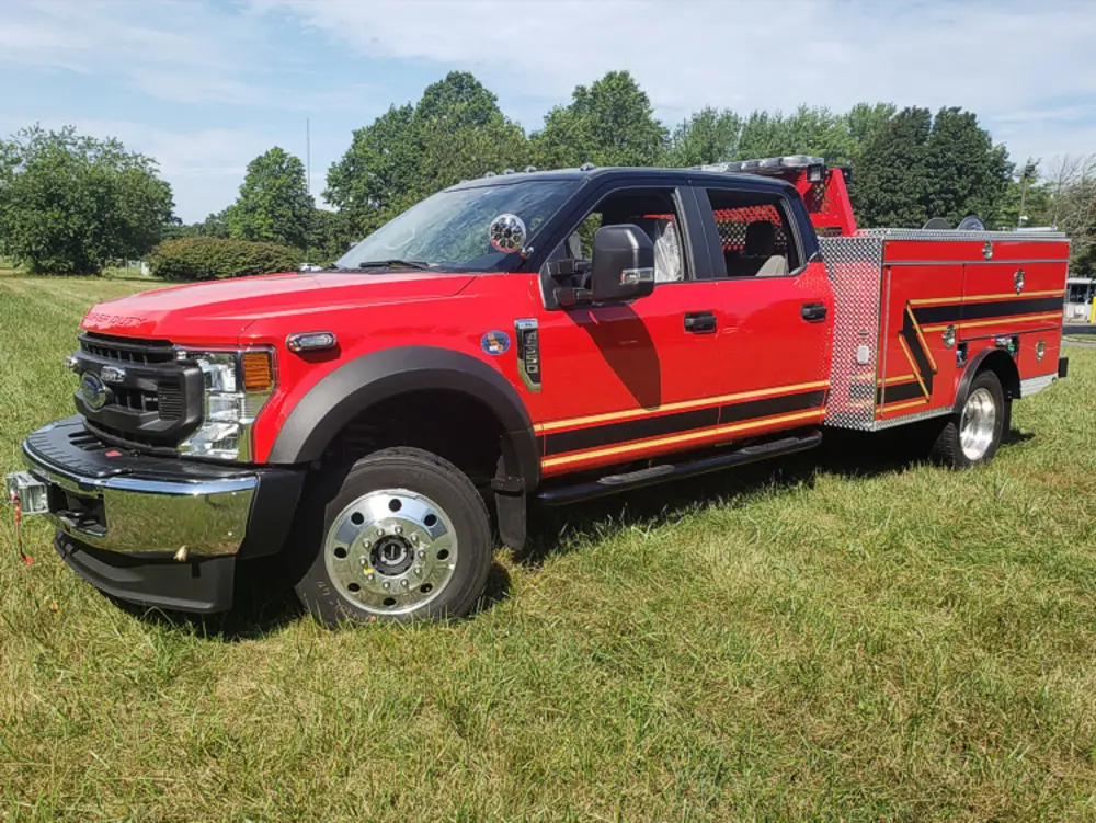 Exterior view of small fire truck showing cab, body compartments, and wheel/tire area.