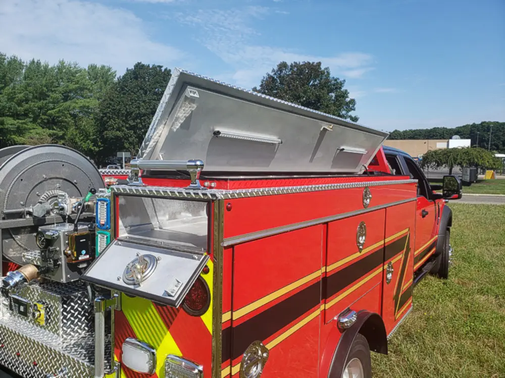 Exterior view of small fire truck showing cab, body compartments, and wheel/tire area.