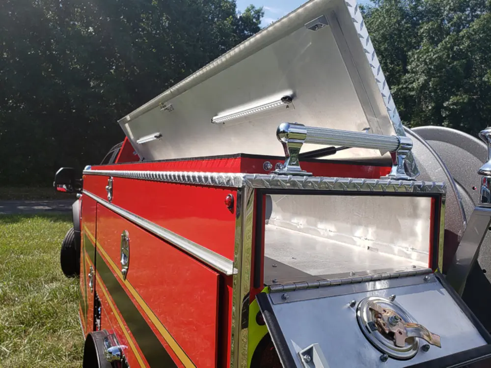 Exterior view of small fire truck showing cab, body compartments, and wheel/tire area.
