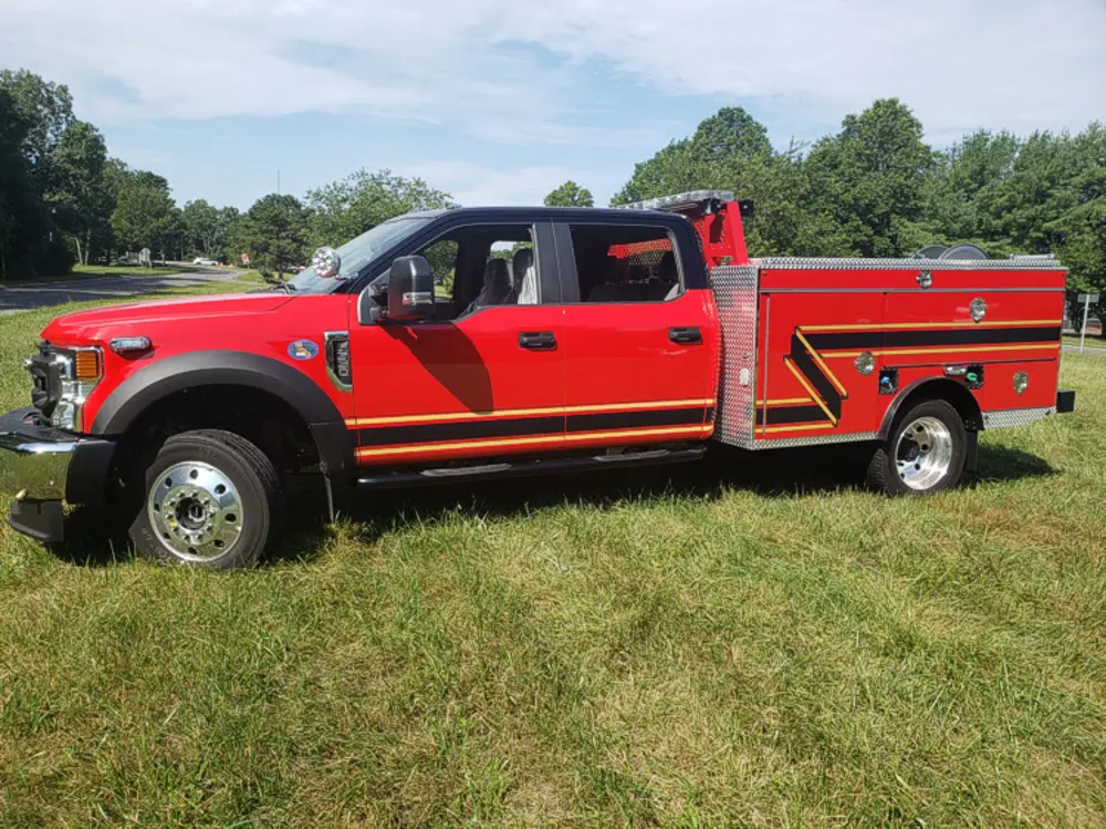 Exterior view of small fire truck showing cab, body compartments, and wheel/tire area.