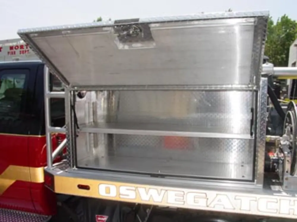 Exterior view of small fire truck showing cab, body compartments, and wheel/tire area.