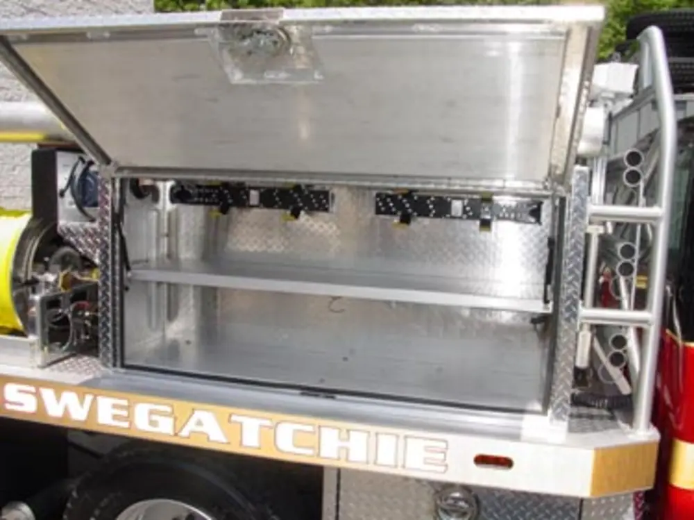 Exterior view of small fire truck showing cab, body compartments, and wheel/tire area.