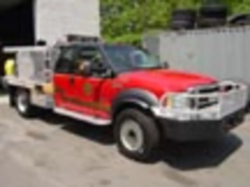 Exterior view of small fire truck showing cab, body compartments, and wheel/tire area.