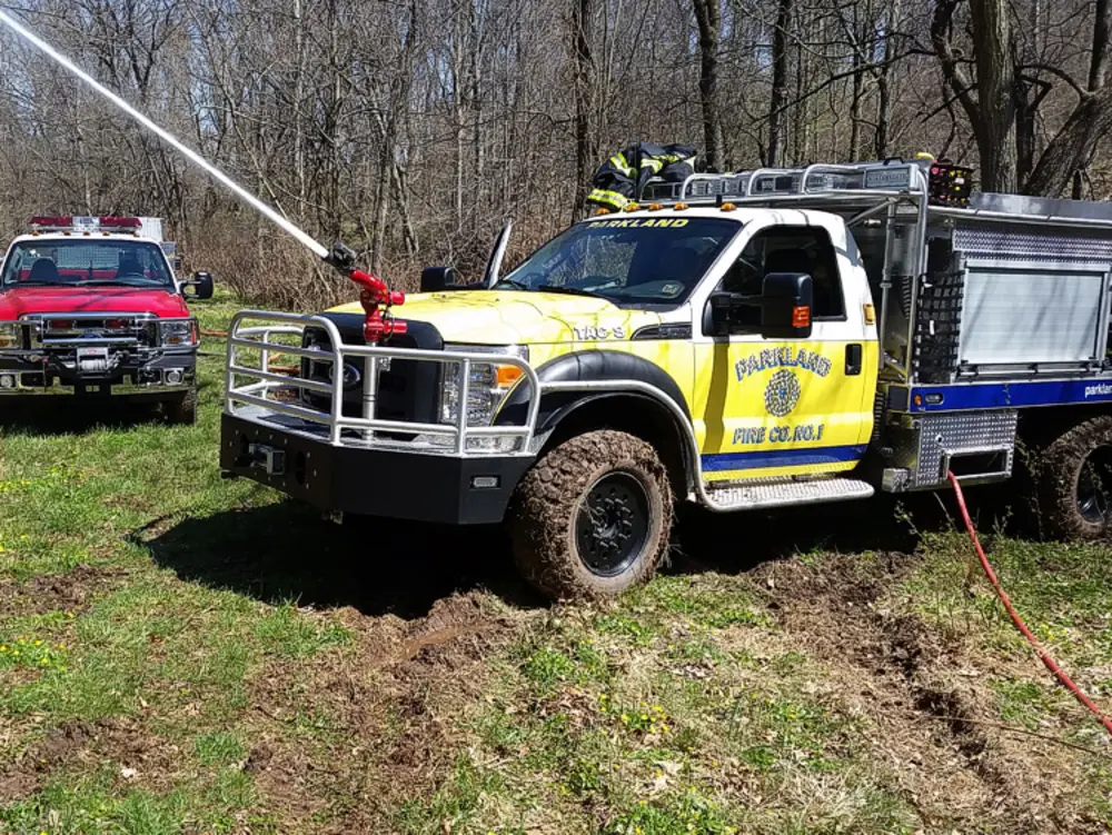 Exterior view of small fire truck showing cab, body compartments, and wheel/tire area.