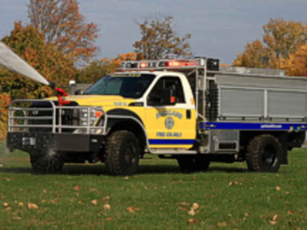 Exterior view of small fire truck showing cab, body compartments, and wheel/tire area.