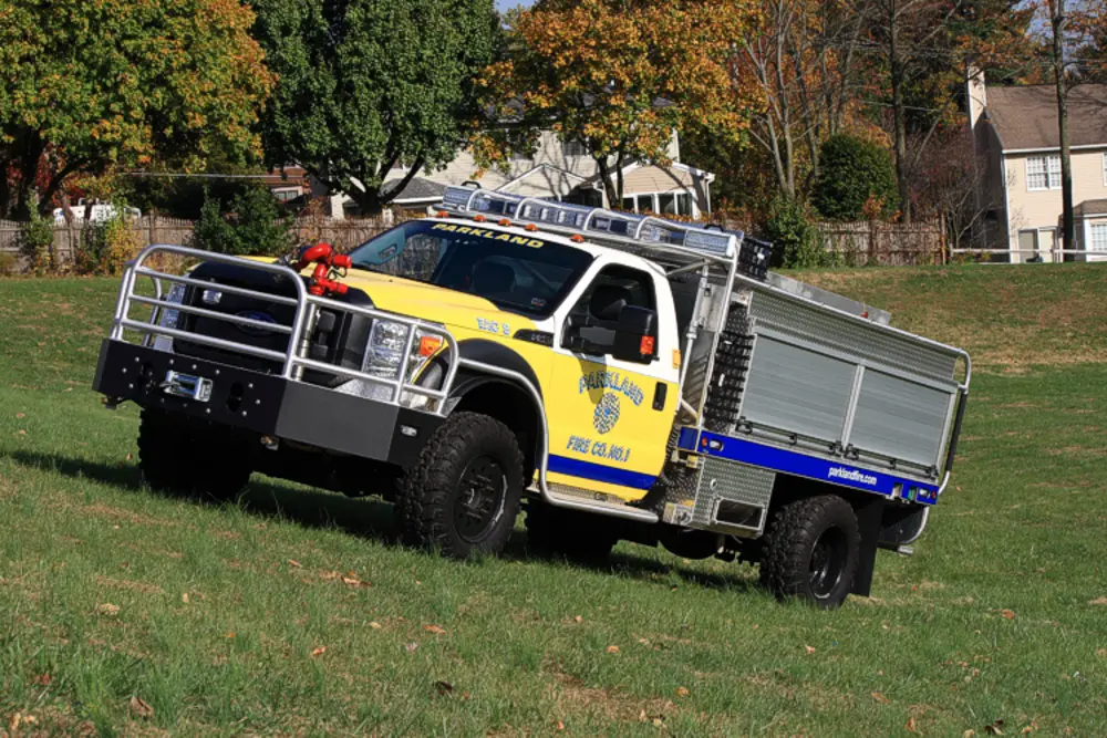 Exterior view of small fire truck showing cab, body compartments, and wheel/tire area.