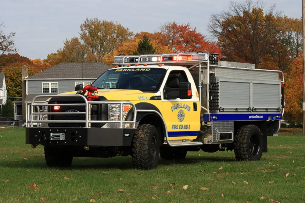 Exterior view of small fire truck showing cab, body compartments, and wheel/tire area.