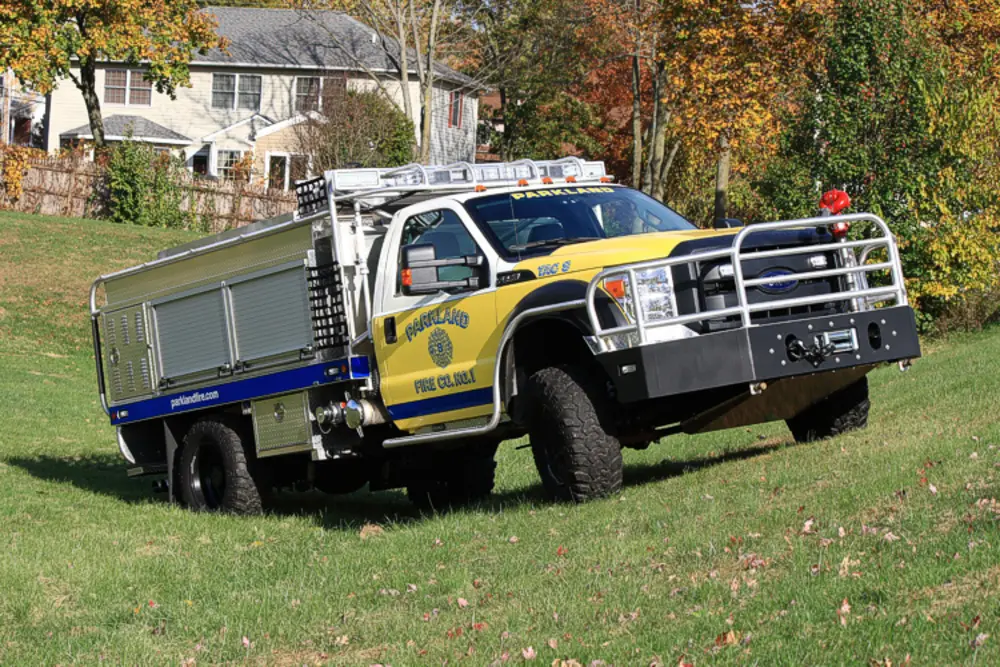 Exterior view of small fire truck showing cab, body compartments, and wheel/tire area.