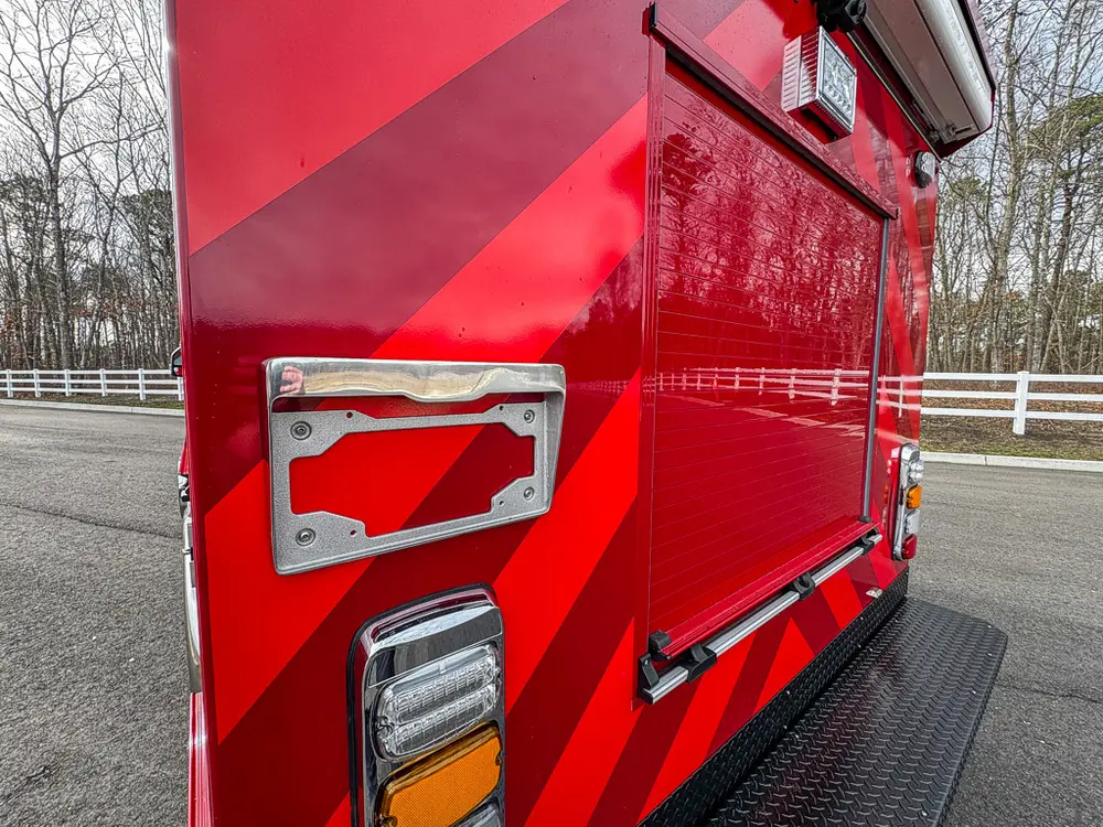 Exterior view of small fire truck showing cab, body compartments, and wheel/tire area.