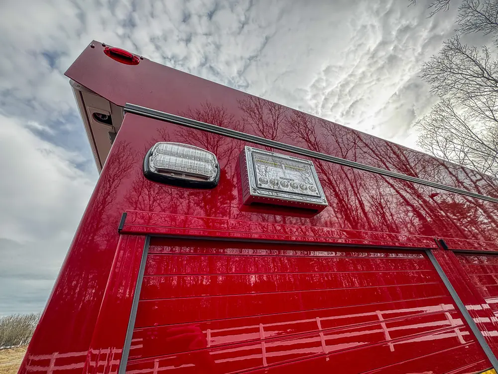 Exterior view of small fire truck showing cab, body compartments, and wheel/tire area.