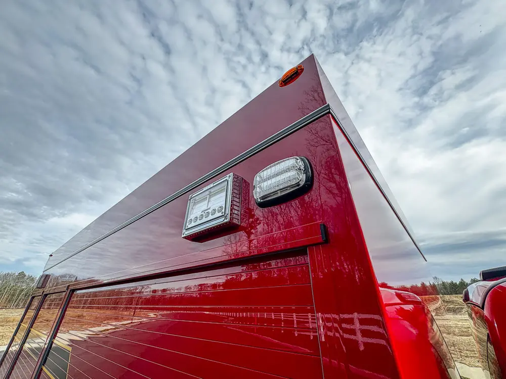 Exterior view of small fire truck showing cab, body compartments, and wheel/tire area.