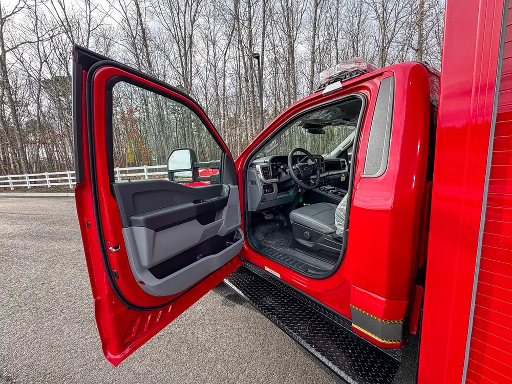 Exterior view of small fire truck showing cab, body compartments, and wheel/tire area.