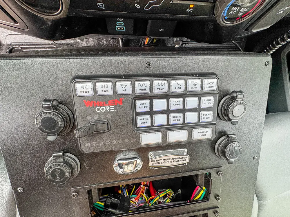Exterior view of small fire truck showing cab, body compartments, and wheel/tire area.