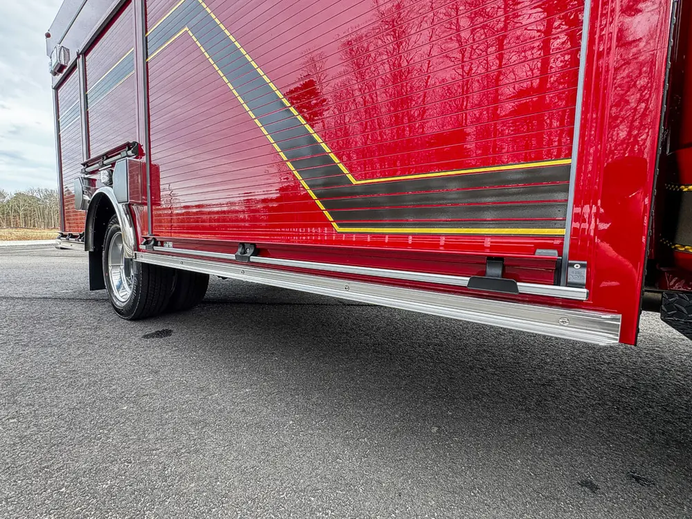 Exterior view of small fire truck showing cab, body compartments, and wheel/tire area.