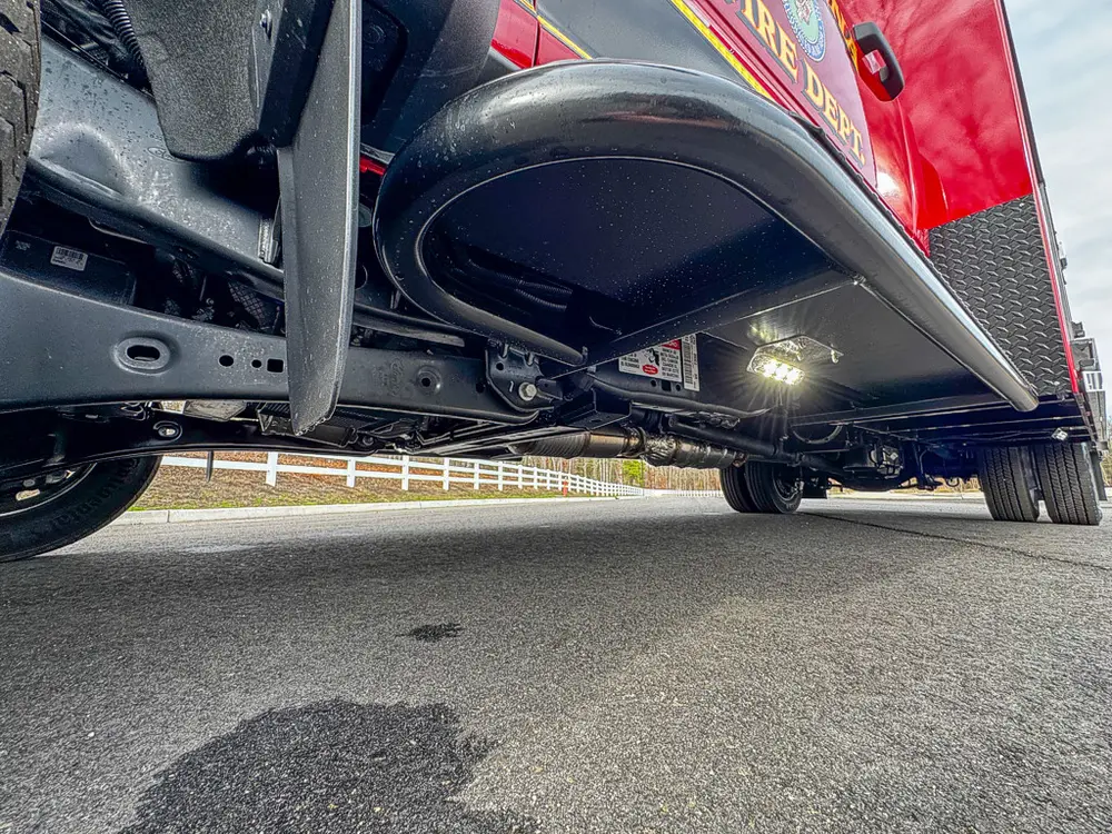 Exterior view of small fire truck showing cab, body compartments, and wheel/tire area.