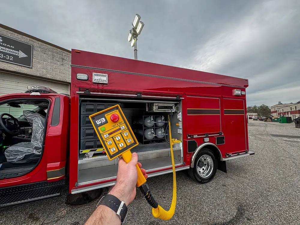 Exterior view of small fire truck showing cab, body compartments, and wheel/tire area.