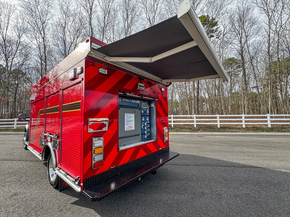 Exterior view of small fire truck showing cab, body compartments, and wheel/tire area.