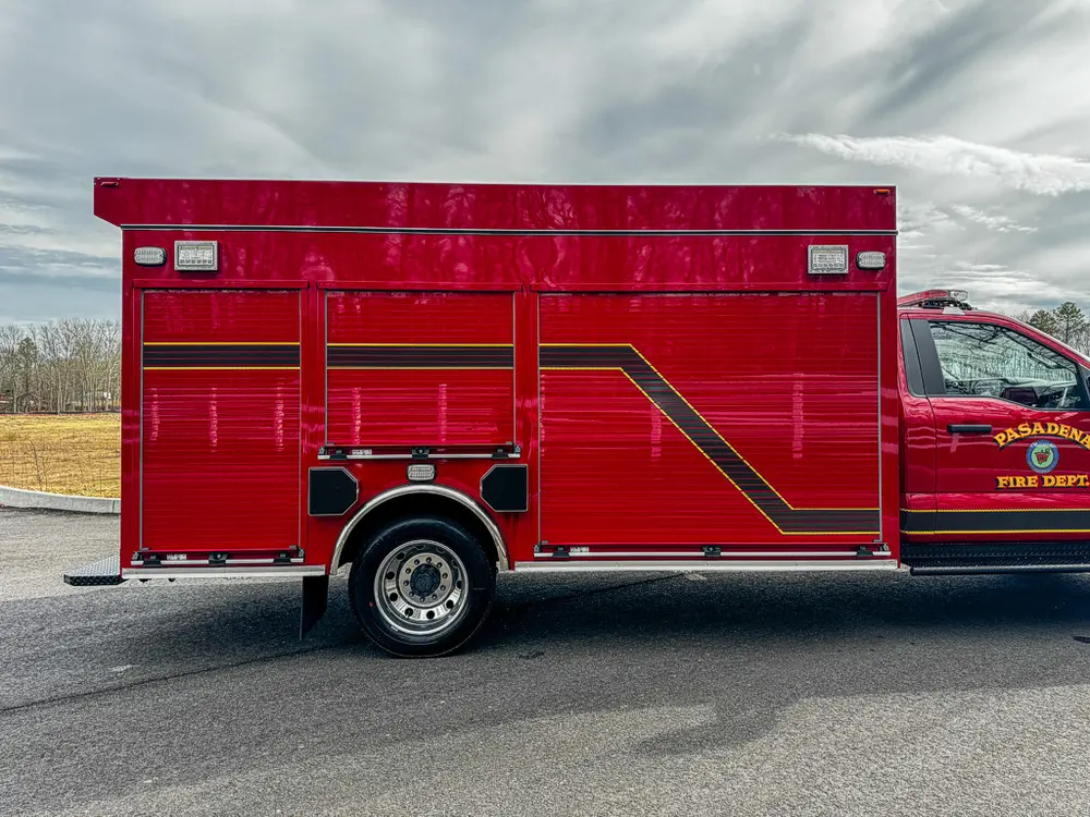 Exterior view of small fire truck showing cab, body compartments, and wheel/tire area.