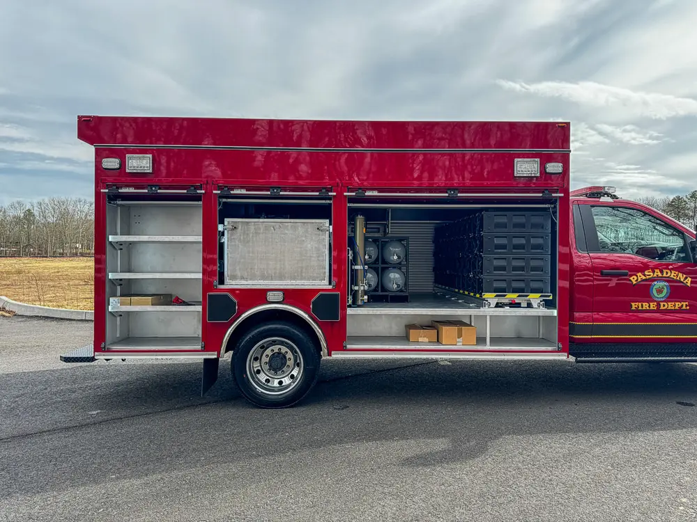 Exterior view of small fire truck showing cab, body compartments, and wheel/tire area.