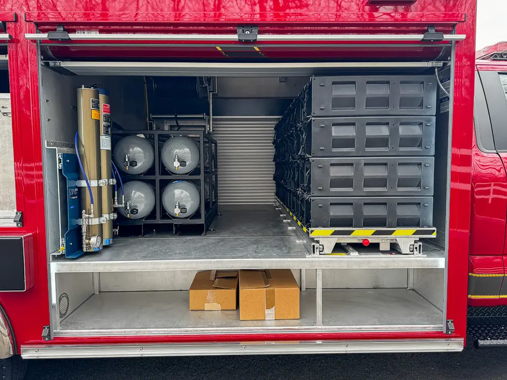 Exterior view of small fire truck showing cab, body compartments, and wheel/tire area.