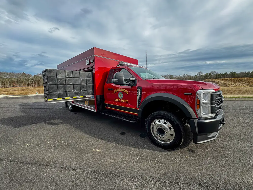 Exterior view of small fire truck showing cab, body compartments, and wheel/tire area.